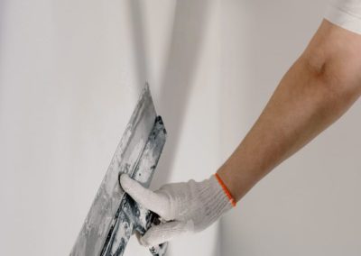 Crop anonymous male worker in gloves holding putty knife while working at home